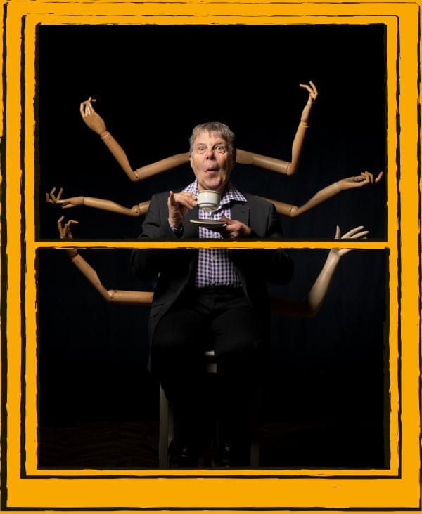 Man sitting on stool, with mannequin arms behind her, on a black background
