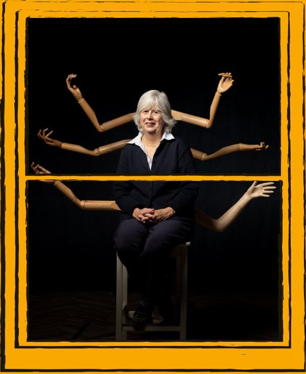 Woman sitting on stool, with mannequin arms behind her, on a black background